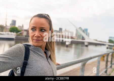 An athletic woman in a grey sweater standing next to the bridge railing. Stock Photo