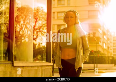 An athletic woman in a grey sweater walking on the street with the sunset in the background. Stock Photo