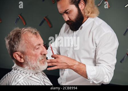 young bearded barber concentrated on working process, close up portrait, hairdresser measuring hair to cut Stock Photo