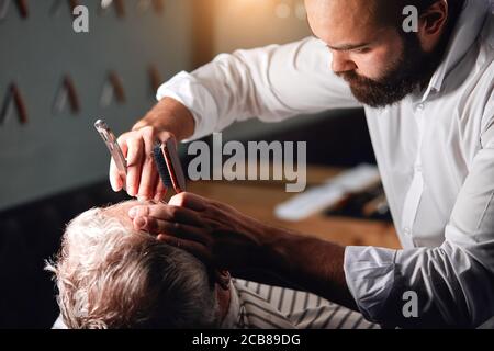pleasant handsome stylist shaving hairs on the forehead of client. close up cropped photo Stock Photo