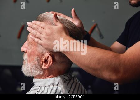 barber styling old man's hair at barbershop, close up side view photo, man's hand touching senior man's hair Stock Photo