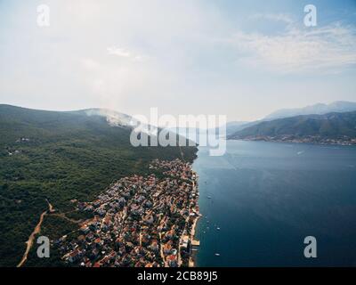 Village Krasici on the Lustica peninsula in Montenegro. The forest fire burns and smokes. The drone flies over residential buildings and villas on the Stock Photo