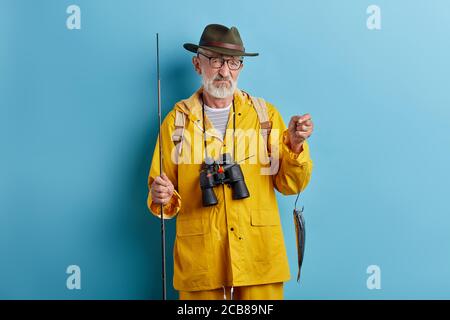 depressed old man is crying . he couldn't catch many fish, close up photo. isolated blue background, studio shot Stock Photo