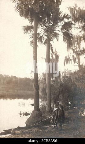 Two girls stand at the water's edge of a swamp with palm trees in the background. Stock Photo