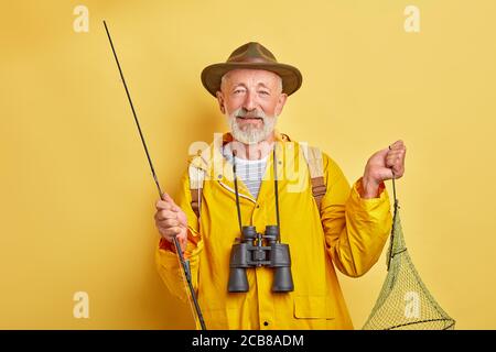 handsome fishman with a fishing pole looking at the camera, close up photo. isolated yellow background. free time activity Stock Photo