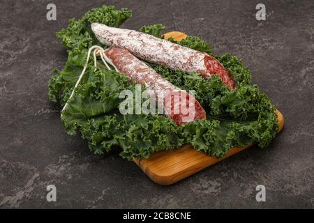 Spanish Fuet sausage with salad leaves over wooden background Stock Photo