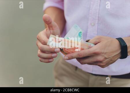 A close up photo of a Caucasian male hand holding a 100 Russian ruble note. Stock Photo