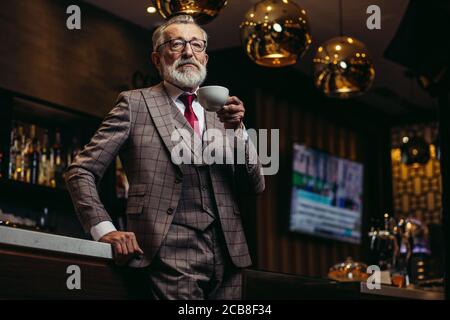 Portrait of wealthy prosperious senior businessman in drinking coffee near bar counter at elite gentlemen club Stock Photo