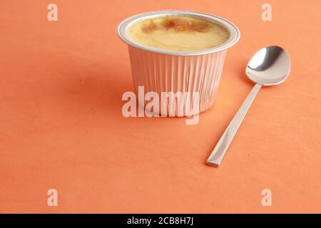 Closeup shot of egg flan in an aluminum container on an orange background Stock Photo