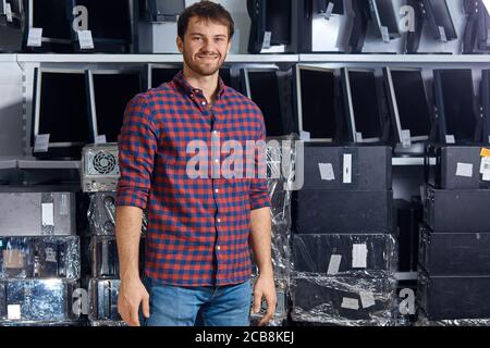 smiling attractive man in checked shirt and jeans posing to the camera in the computer office, close up photo. young man having a rest after repairing Stock Photo
