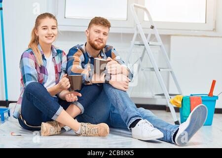 Young family of house decorators chilling in empty room prepared for painting, sitting between tools, that are always needed during repair time instru Stock Photo