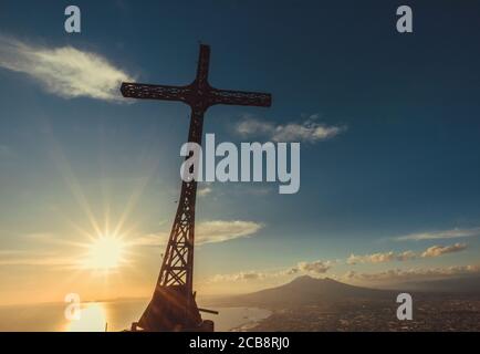 Cross  made of steel standing over the gulf of Naples, with view of the Mount vesuvius and Sunset with warm light. Stock Photo