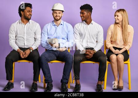 multicultural project group sitting and looking at construction engineer in safety helmet. Construction Concept Stock Photo