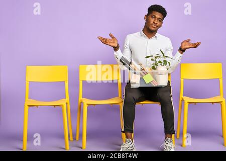 sad young dark-skinned man holding box of personal belongings quit job Stock Photo