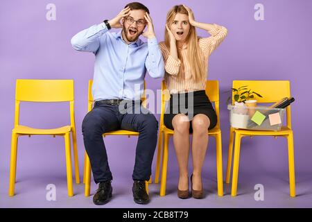 excited and shocked young man in round eyewear and blonde woman received unbelievable news, sitting and touching heads and waiting for job interview Stock Photo