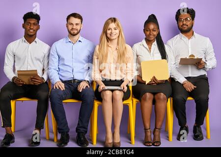 group of multicultural young people sitting straight and looking in camera waiting for job interview Stock Photo