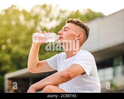 Young Caucasian man resting and drinking water after an outdoors workout Stock Photo