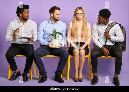 multiethnic men flirting with young pretty blonde woman in glasses waiting for job interview Stock Photo