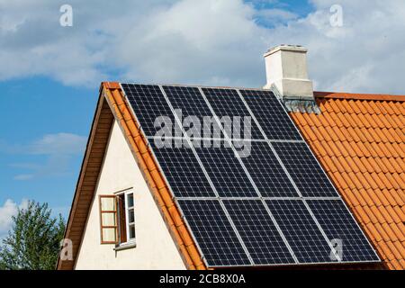 Modern black solar panels on the red tile roof of an old house with blue sky background. Stock Photo