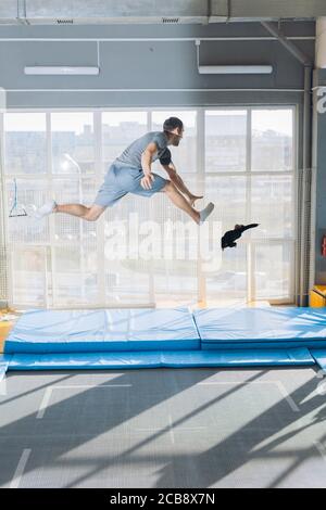 active crazy guy is tryng to catch falling toy while jumping on the trampoline. full length side view shot.copy space Stock Photo