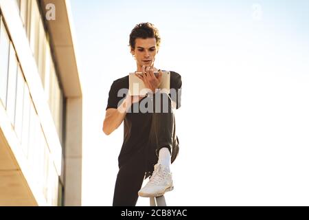 Handsome young man using digital tablet while sitting on railing against clear sky Stock Photo