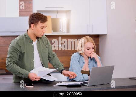 Finance managers task. young caucasian woman and man use laptop computer and document paper, sit on table and discuss Stock Photo