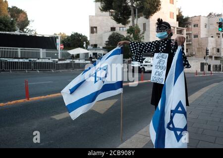 Jerusalem, ISRAEL - AUGUST 11th 2020: A lone pro-Netanyahu counter-protester holds Israeli flags across a buffer zone set up by police to separate Pro-Netanyahu supporters from anti-Netanyahu protesters demonstrating outside the Prime Minister's official residence on August 11, 2020 in Jerusalem, Israel. Israelis have taken to the streets in almost daily demonstrations calling for Netanyahu's resignation over his corruption charges, accused mismanagement of the coronavirus crisis and his assault on democracy. Stock Photo