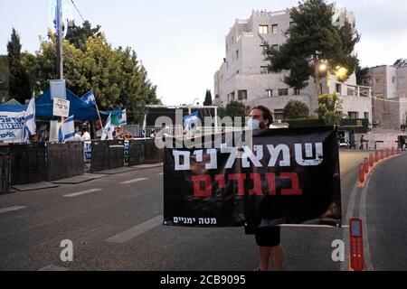 Jerusalem, ISRAEL - AUGUST 11th 2020: Pro-Netanyahu counter-protester holds up a banner which reads 'Leftists are traitors' across a buffer zone set up by police to separate Pro-Netanyahu supporters  from anti-Netanyahu protesters demonstrating outside the Prime Minister's official residence on August 11, 2020 in Jerusalem, Israel. Israelis have taken to the streets in almost daily demonstrations calling for Netanyahu's resignation over his corruption charges, accused mismanagement of the coronavirus crisis and his assault on democracy. Stock Photo