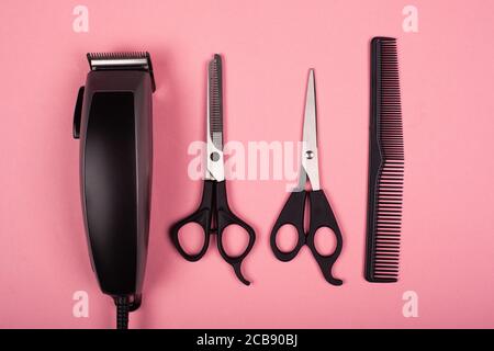 hairdressing tools, hair cutting tools, hair clipper and scissors on pink background top view. Stock Photo