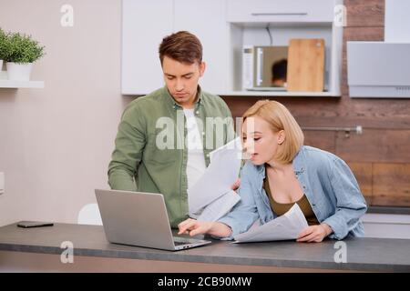 spouses sitting with modern laptop and documents, analyzing paperwork and house utility bills, young couple consider papers managing finances and expe Stock Photo