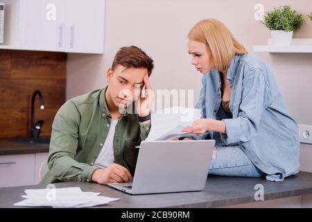 thoughtful couple solving financial problems in family, using laptop, holding paper documents, discussing costs for past month Stock Photo