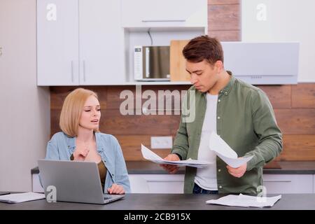 spouses sitting with modern laptop and documents, analyzing paperwork and house utility bills, young couple consider papers managing finances and expe Stock Photo