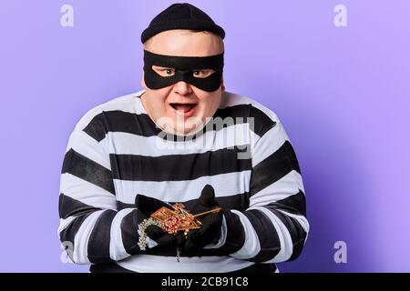happy smiling burglar has found adornment, decoration, ornament in the flat. isolated blue background. studio shot Stock Photo