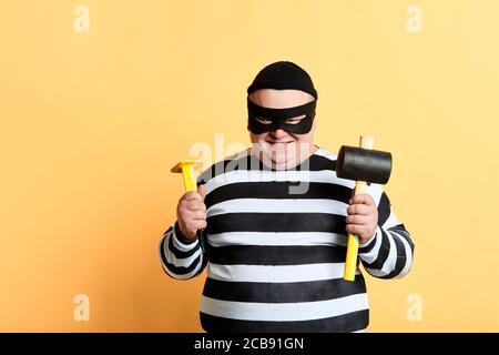 plump thief with hammer standing isolated on yellow background, close up portrait Stock Photo