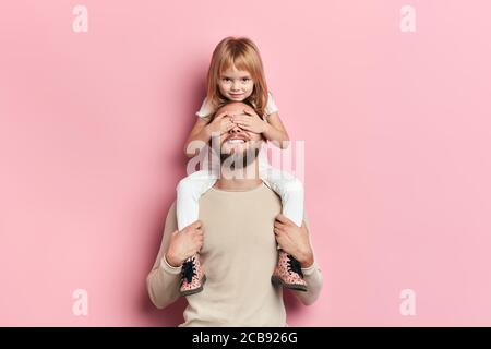 funny crazy naughty smiling girl closing her father's eyes with a while sitting on the shoulder of her daddy. close up portrait, happiness Stock Photo