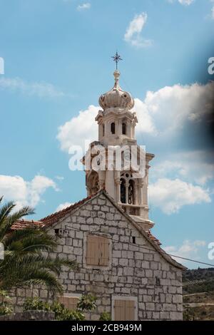 Tall belltower in a tiny village of Lozisca on the island of Brac, Croatia. Beautiful christian tower rising above the old buildings Stock Photo