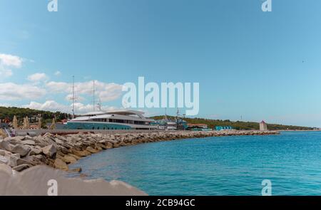 View of large yachts docked in the port of Postira, small town on the island of Brac in Croatia. Warm summer day, beautiful bright blue sea and sky. P Stock Photo