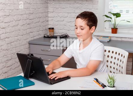 Child using laptop while sitting at desk with book and doing homework Stock Photo