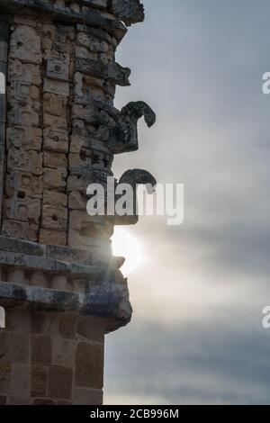 The sun behind the carved stone Chaac masks with their curling noses on the corner of the north building of the Nunnery Quadrangle in the pre-Hispanic Stock Photo