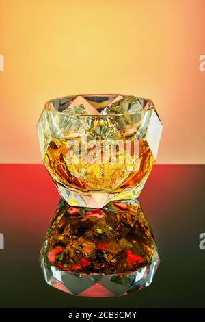 Crystal goblet with elite whiskey and ice cubes on a gradient background with reflection. Stock Photo