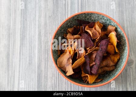 Sweet potato, beetroot and parsnip crisps chips in a patterned bowl.  Grey wood background Stock Photo