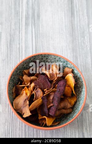 Sweet potato, beetroot and parsnip crisps chips in a patterned bowl.  Grey wood background Stock Photo