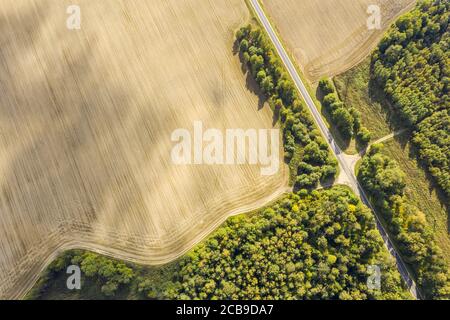 aerial top view of country road through green forest and ploughed fields on bright summer day Stock Photo