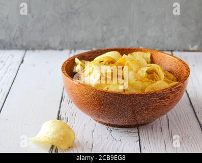Potato chips or crisps in wooden bowl against white wooden background. Pile of potato chips. Potato chips is snack. Top view Stock Photo
