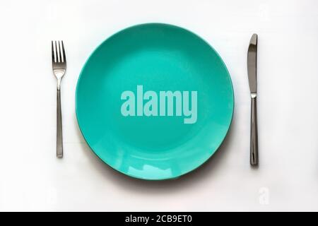 Clean green plate and stainless knife and fork isolated on white background. Served cutlery. Top view Stock Photo