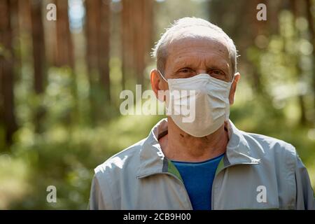 an elderly man in a protective mask walks in the Park, a walk in the fresh air after quarantine, a precautionary measure against the virus Stock Photo