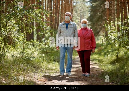 an elderly couple in protective masks walking in the Park, a walk in the fresh air after quarantine, a precaution against the virus Stock Photo