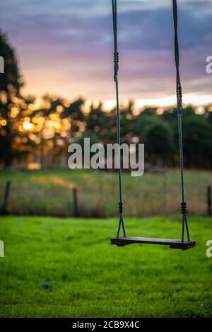Nostalgic Wood and Rope Swing in a Rural Garden With Meadow and Forest at Sunset in the Background Stock Photo