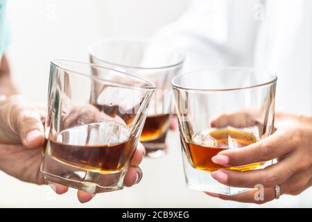 Group of friends toasting with glasses of whiskey brandy or rum indoors - closeup Stock Photo