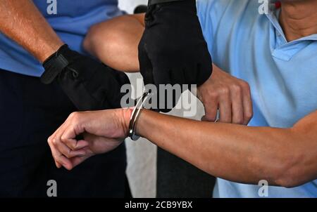12 August 2020, Saxony, Chemnitz: Judicial officers are removing the handcuffs from a man accused of double murder at Chemnitz Regional Court. The accused is said to have strangled two brothers with an electric cable in their apartment in the summer of 1995. The victim and perpetrator were Vietnamese. The background of the crime was illegal cigarette trade and protection racket. After the murder, the man had left for the Czech Republic, where he had lived under false identity. Last year he was arrested in Prague and transferred to Germany. Photo: Hendrik Schmidt/dpa-Zentralbild/dpa Stock Photo